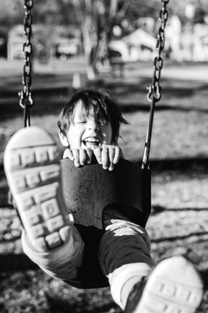 Black and white photo of little boy on Swing in playground photo session